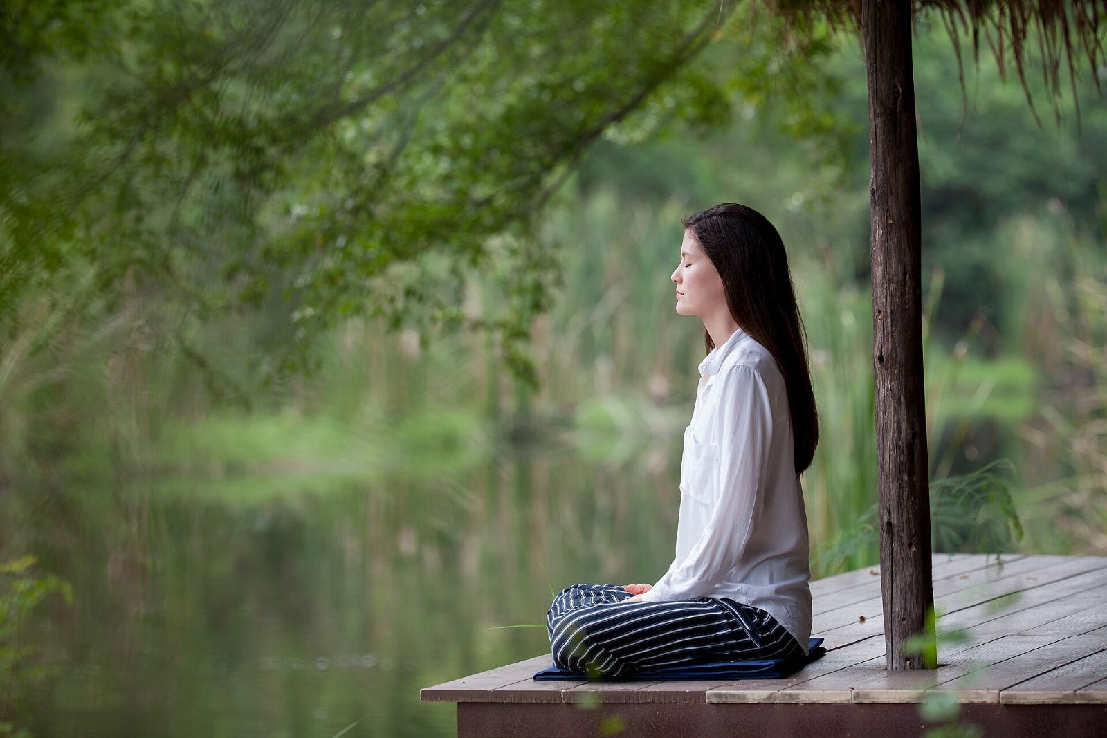 A woman meditating on a wooden deck by a quiet pond